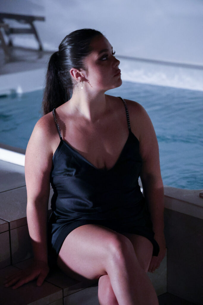Woman in black dress sitting by a pool during a milestone photography session
